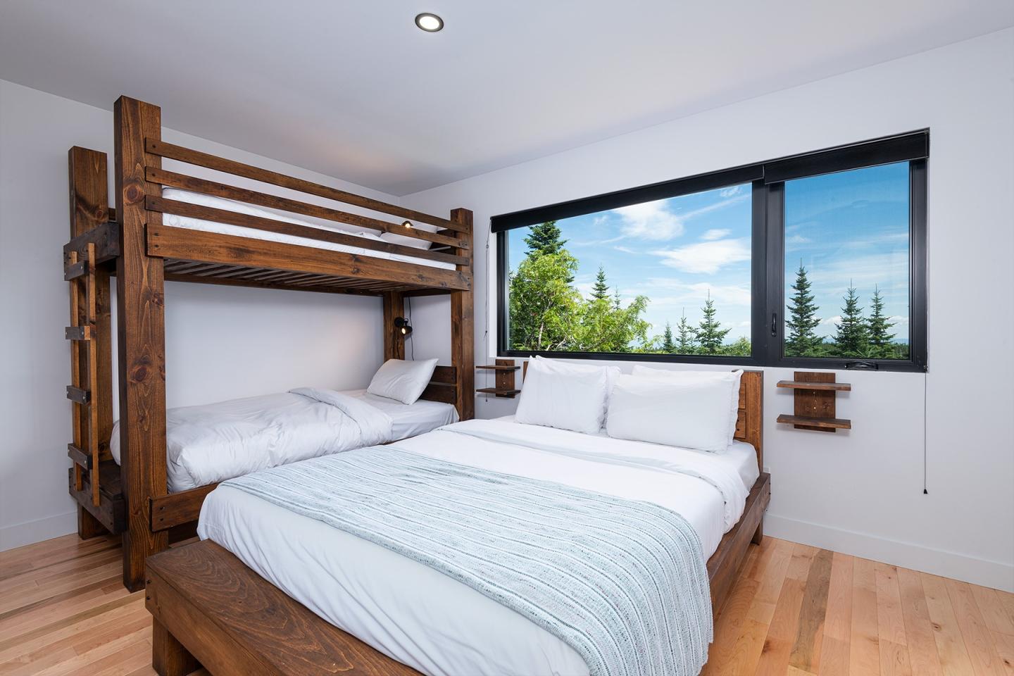 Chambre lumineuse avec lits superposés en bois et vue sur forêt.