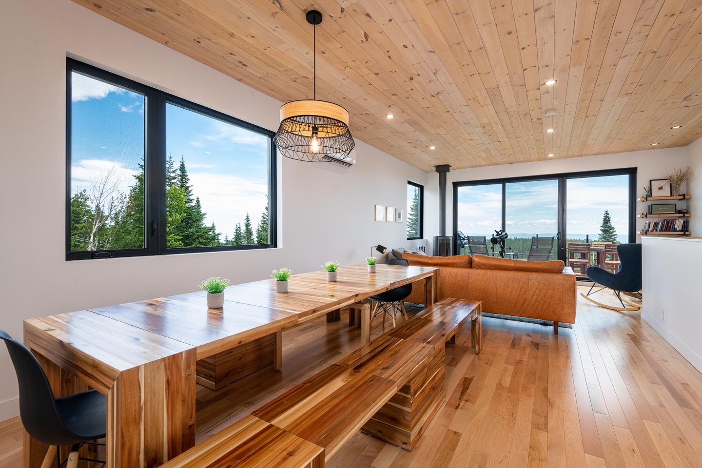 Salle à manger moderne avec table en bois massif, chaises noires et vue sur la forêt.