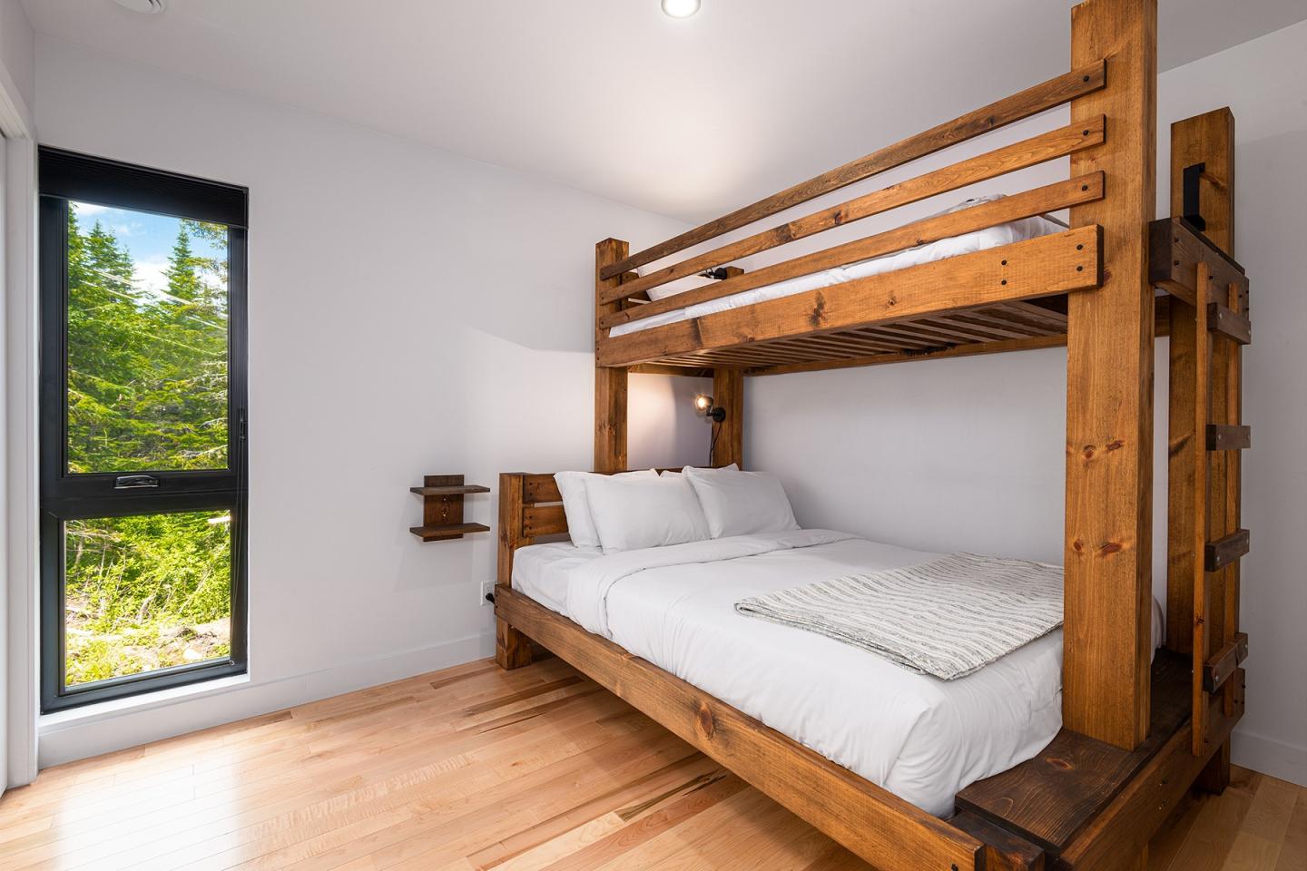 Lit superposé en bois dans une chambre lumineuse avec fenêtre sur la forêt.