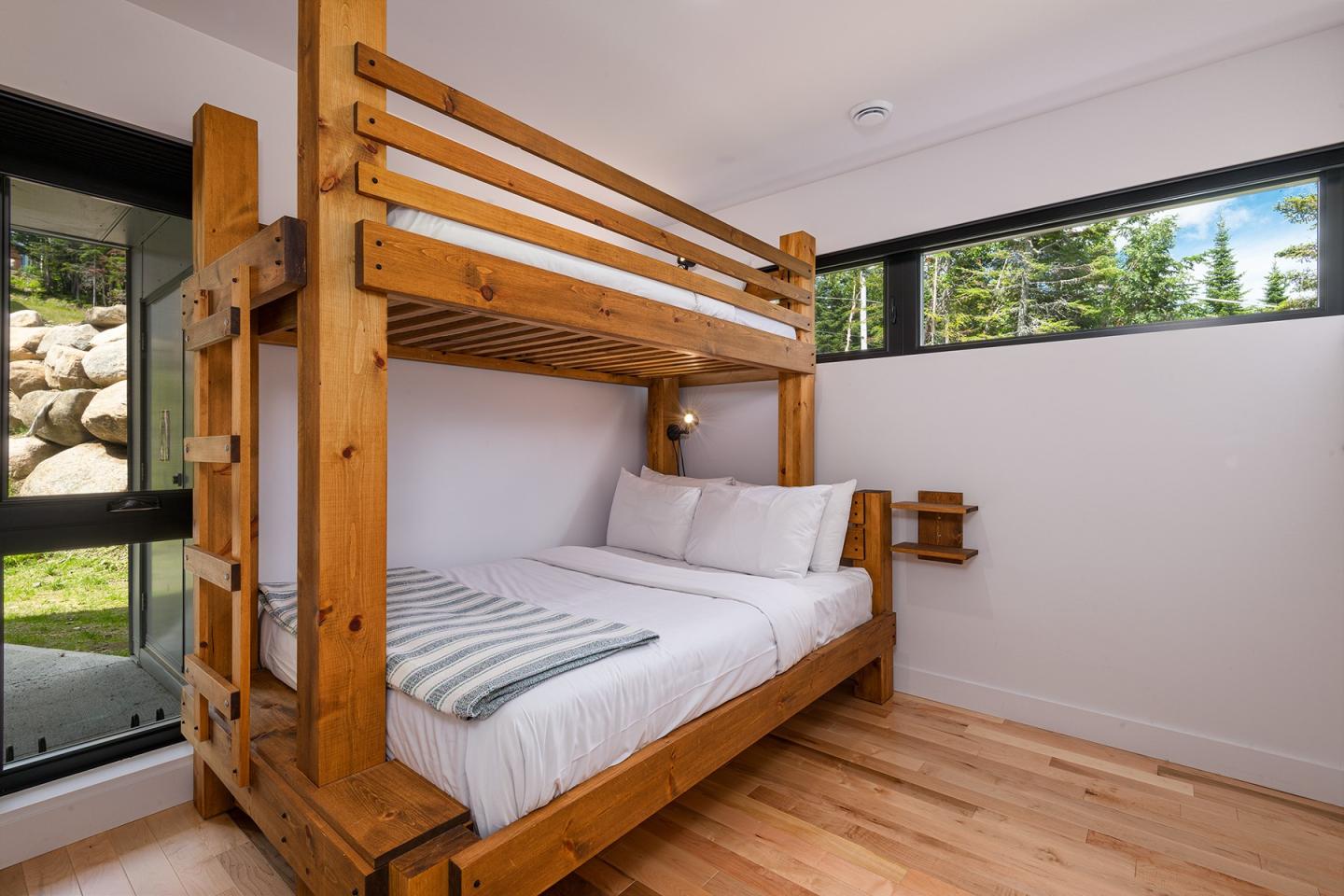 Chambre avec lit superposé en bois, grandes fenêtres, parquet clair.