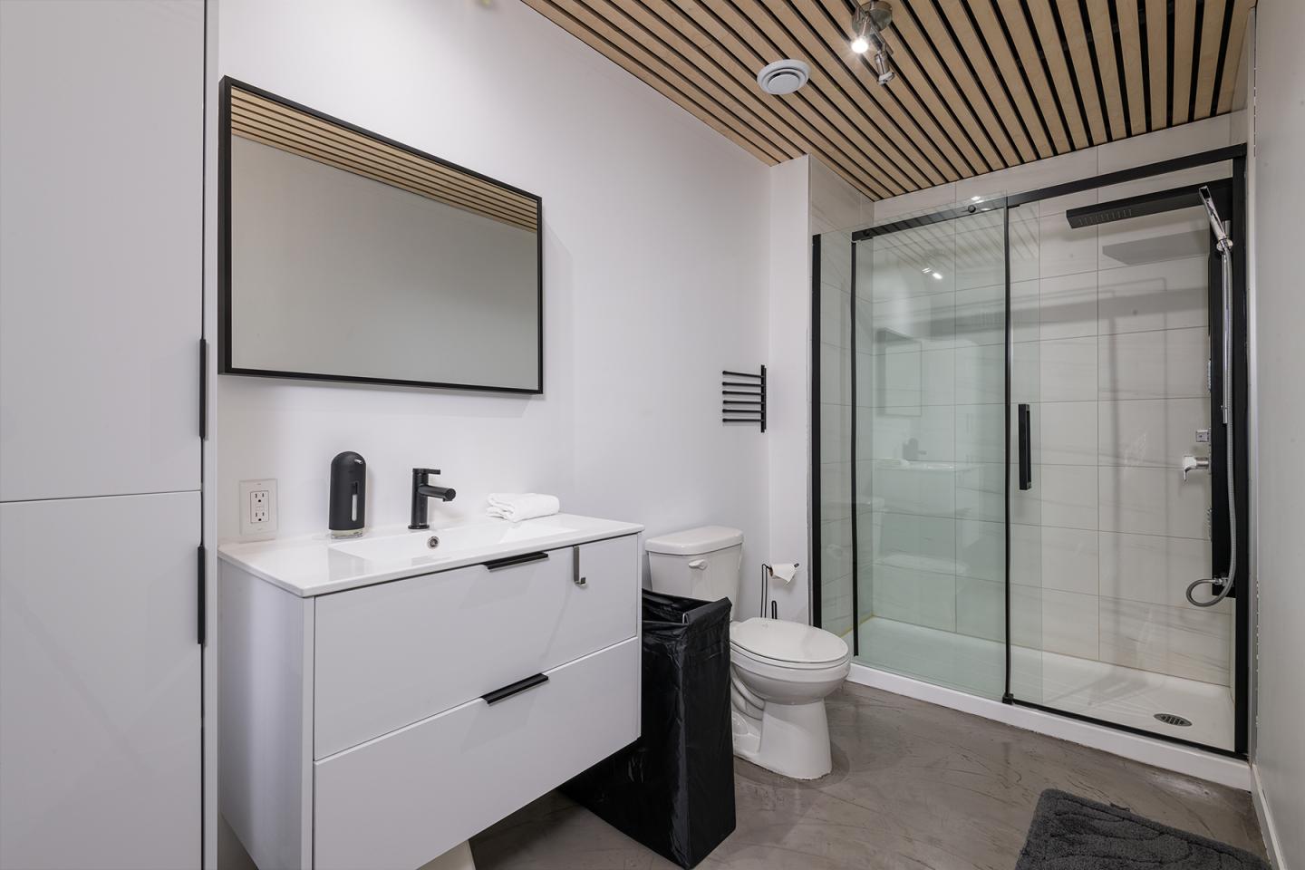 Salle de bain moderne avec douche vitrée, meuble blanc et miroir.