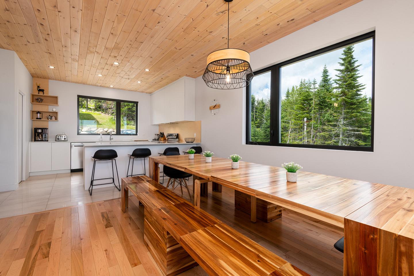 Grande salle à manger en bois avec vue sur la forêt par la fenêtre.