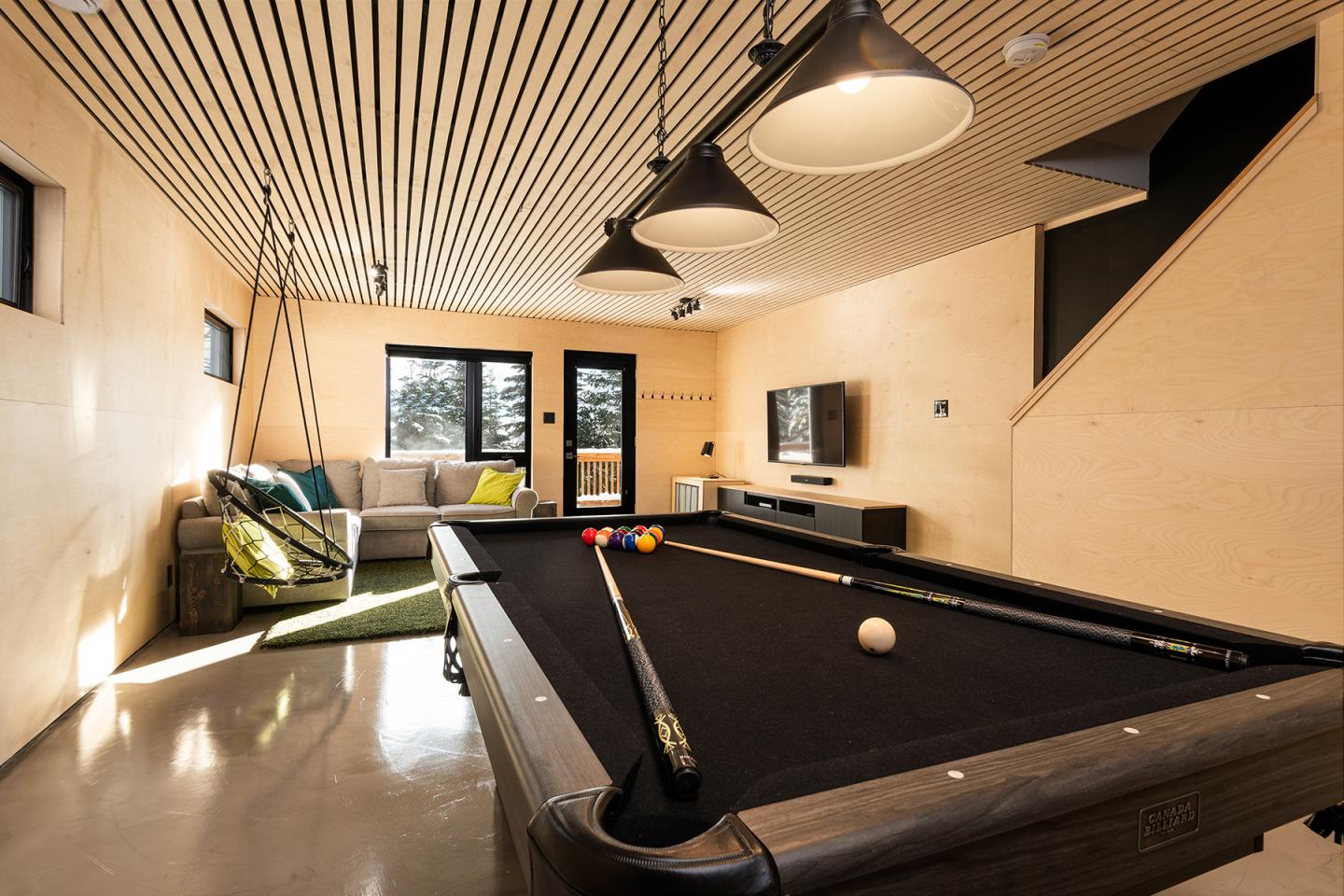 Salle de jeux moderne avec table de billard, canapé et éclairage suspendu.