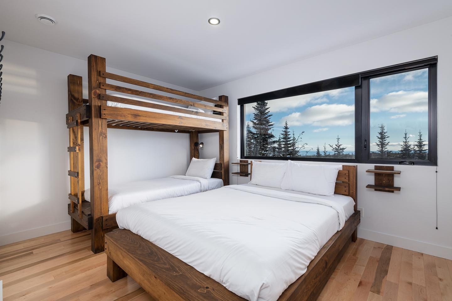 Chambre avec lits superposés en bois, vue sur forêt par la fenêtre.