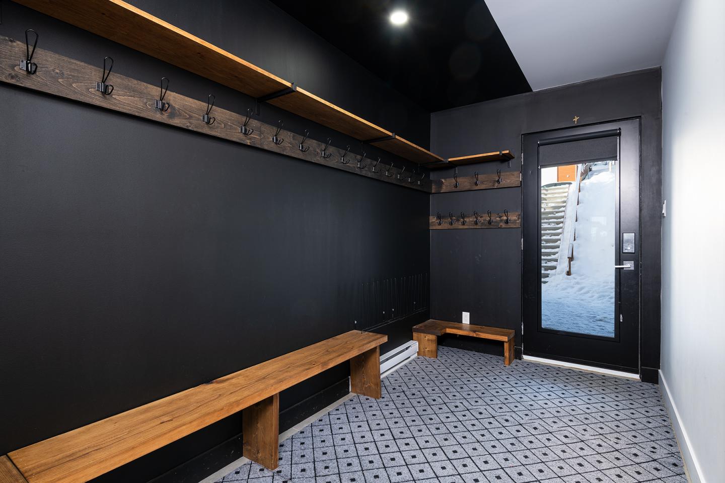 Vestiaire moderne avec bancs en bois, murs noirs et porte-fenêtre.
