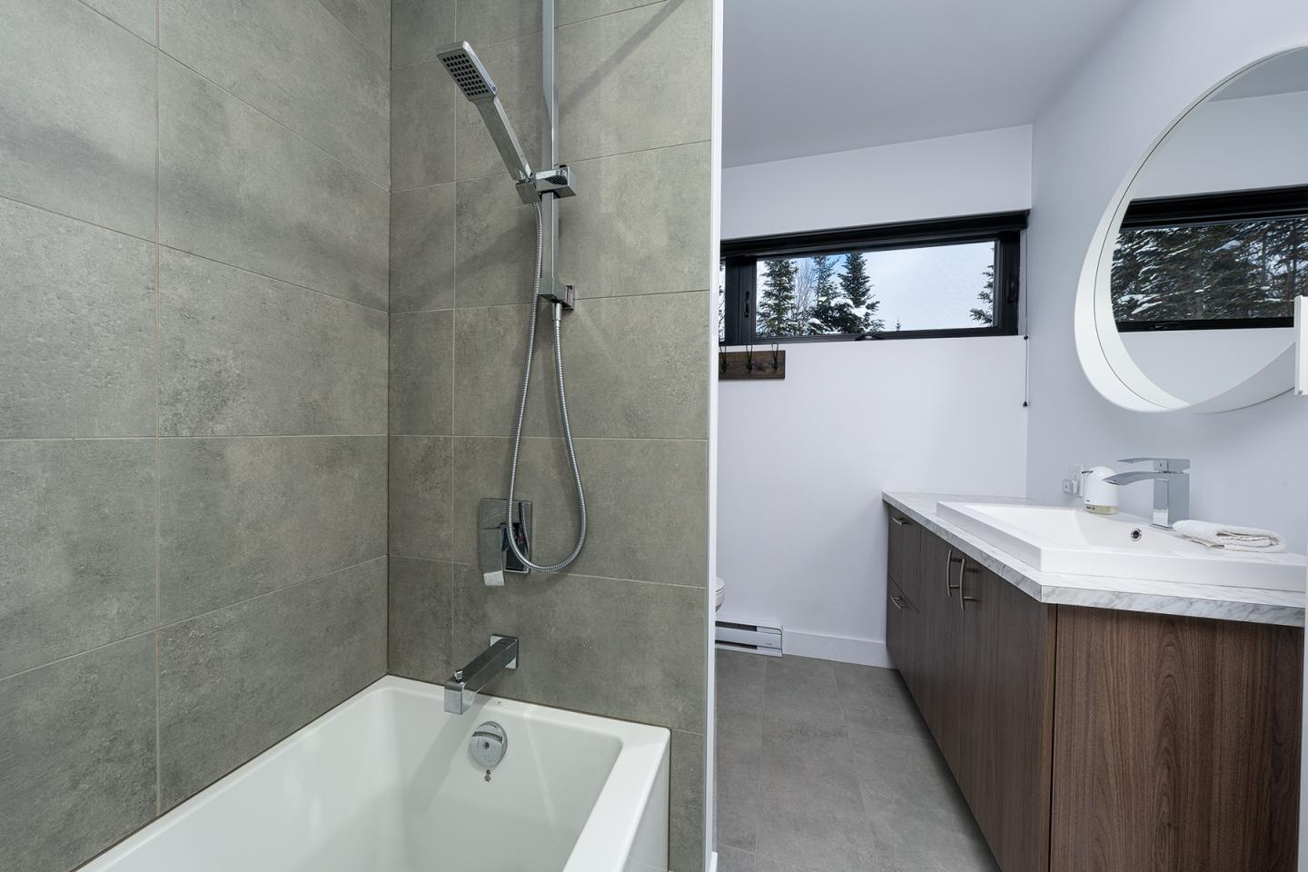 Salle de bain moderne avec douche, baignoire et meuble en bois clair.