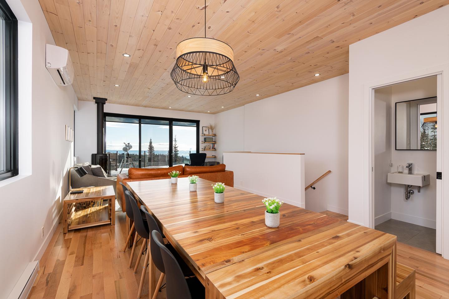 Salle à manger moderne, table en bois, lumière naturelle, vue sur mer, plafond en bois.
