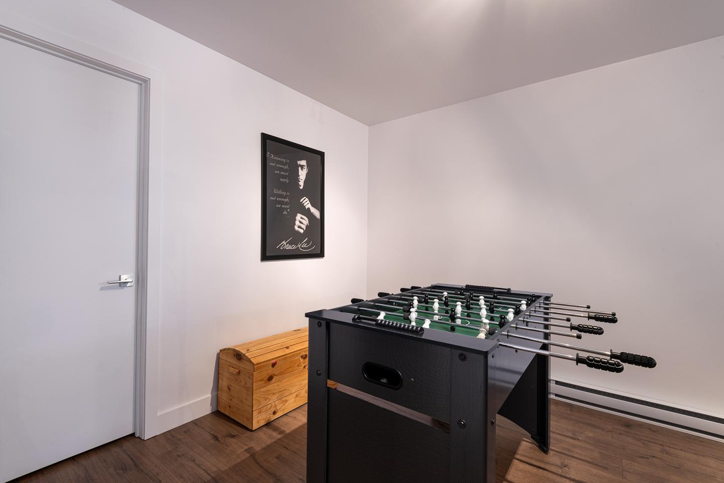 Baby-foot dans une salle moderne, avec banc en bois et affiche au mur.