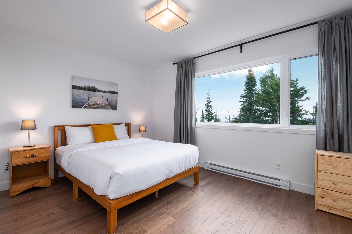 Chambre minimaliste avec lit double, grande fenêtre et deux tables de chevet.