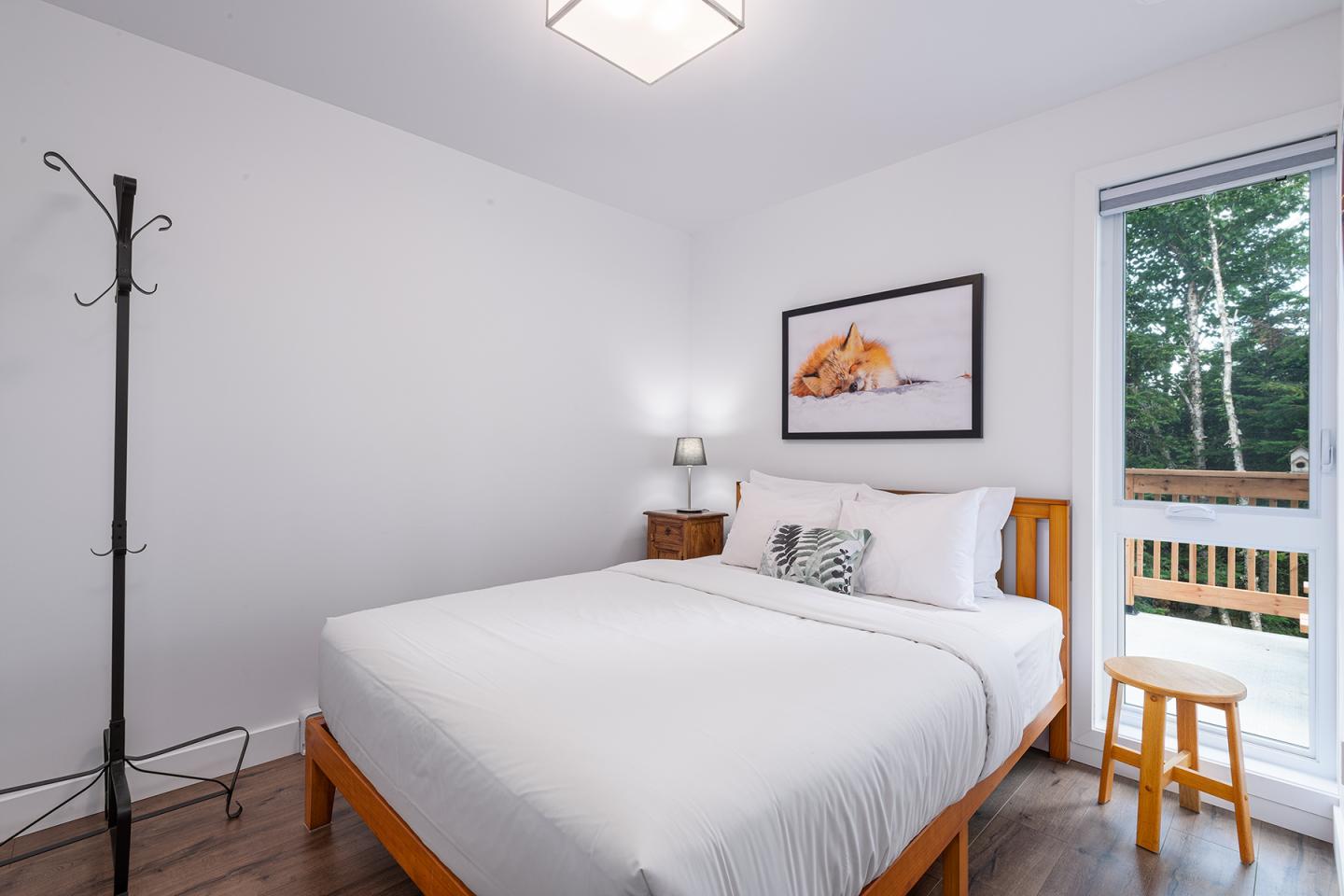 Chambre lumineuse avec un lit double, cadre mural, et vue sur balcon.