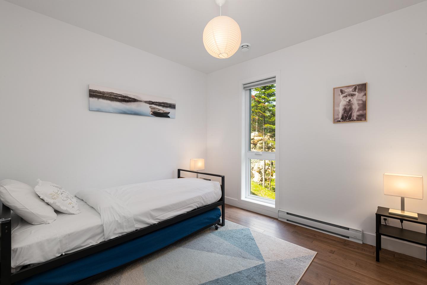 Chambre lumineuse avec lit simple, lampes de chevet et fenêtre sur jardin.