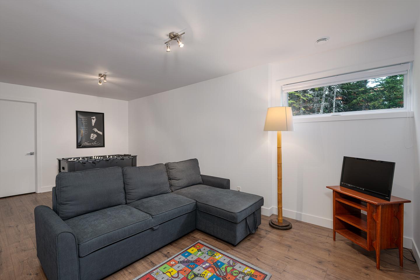 Salon moderne avec canapé gris, lampe sur pied, et petite télé.