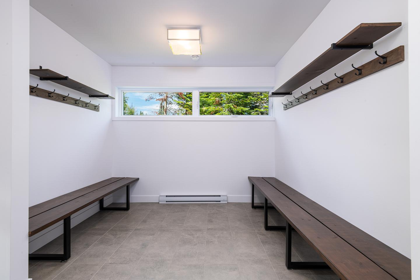 Vestiaire avec bancs en bois et murs blancs. Fenêtres en hauteur.