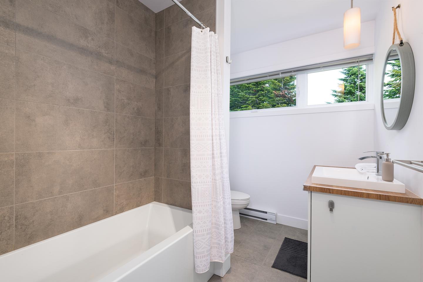 Salle de bain moderne avec baignoire, rideau blanc et vasque sur meuble en bois clair.