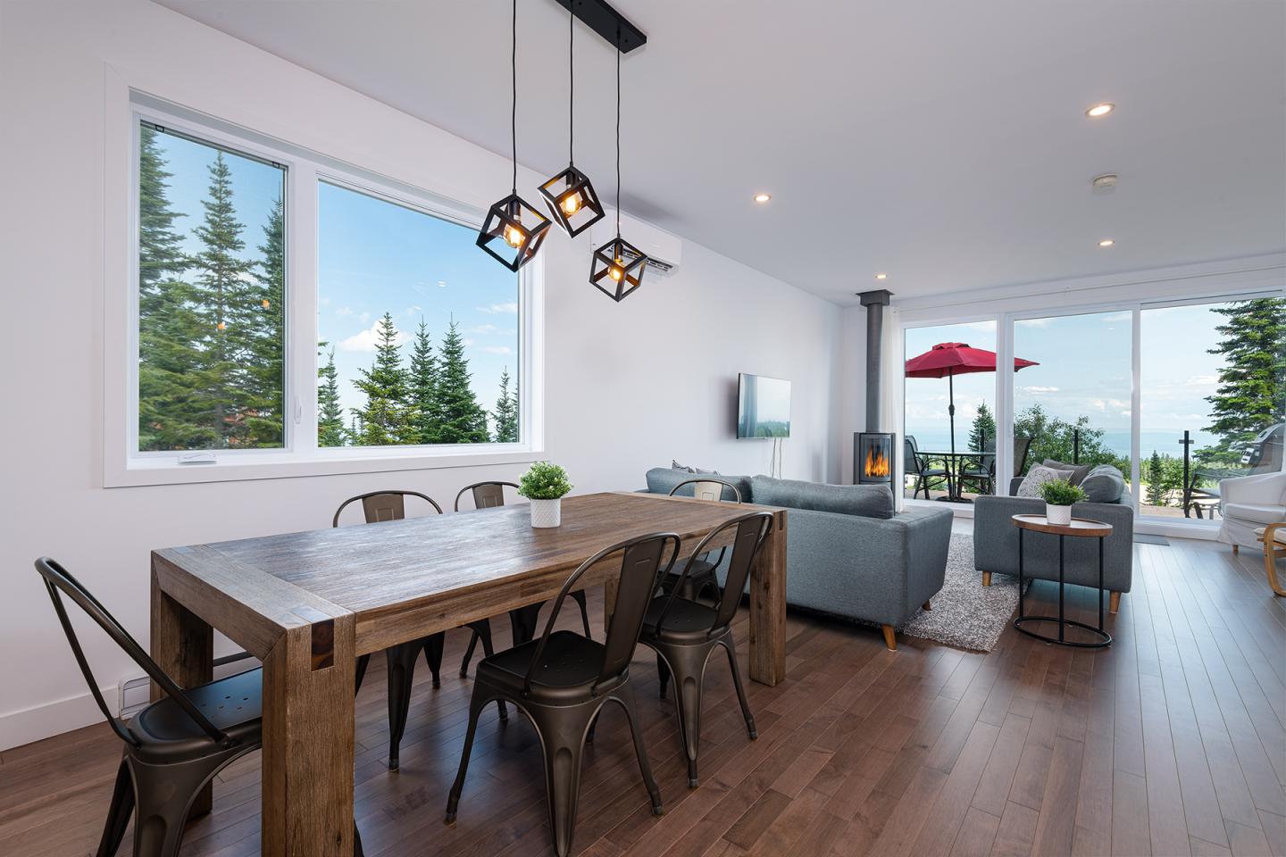 Salle à manger moderne avec table en bois, fenêtres donnant sur la forêt.