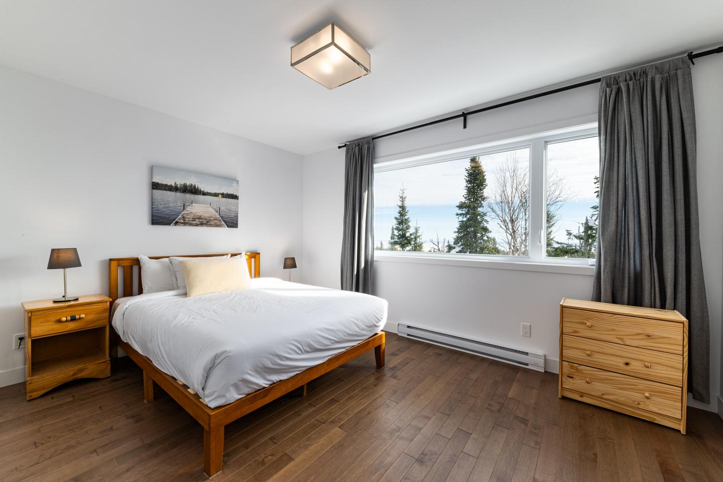 Chambre lumineuse avec lit double et grande fenêtre sur des arbres.