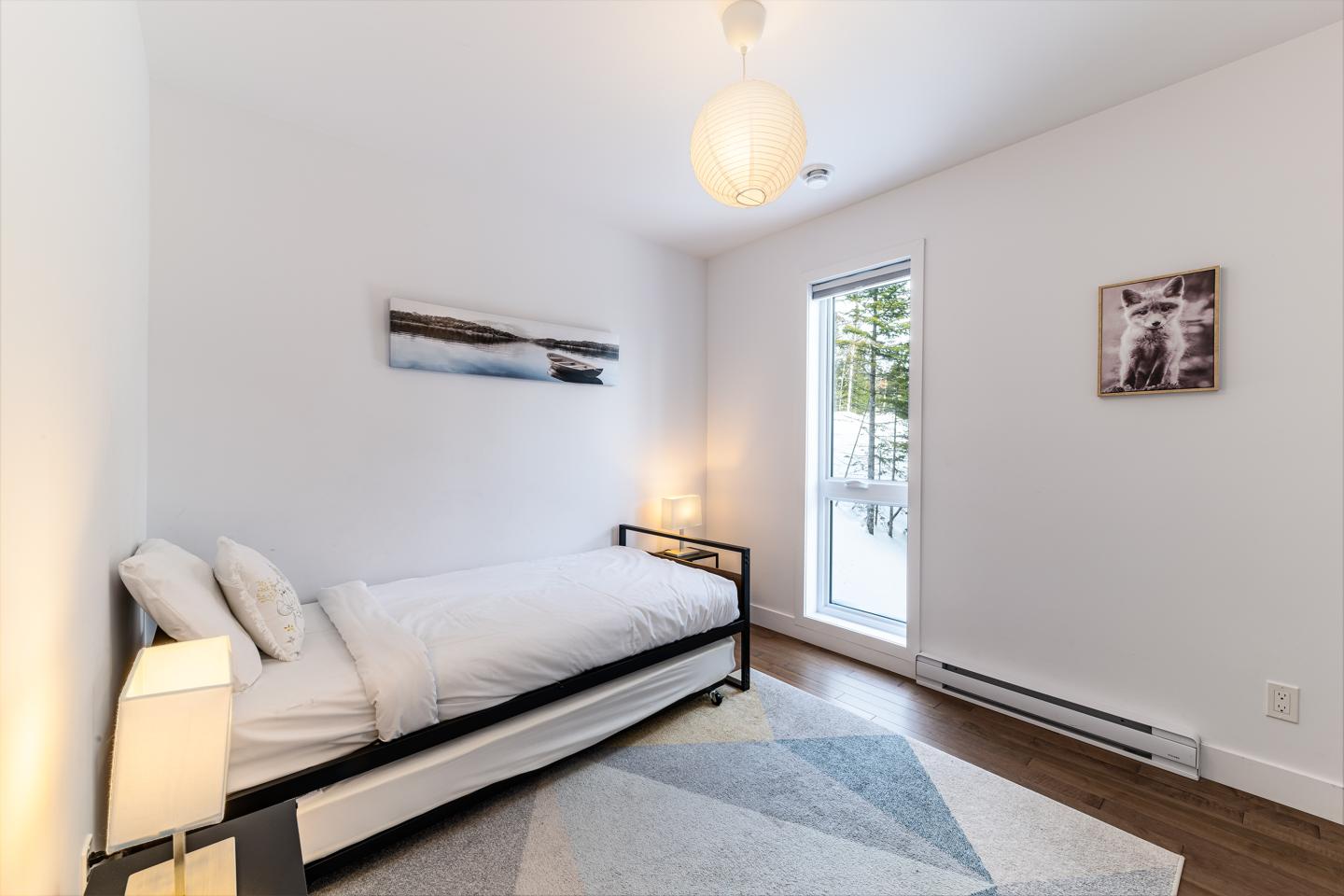 Chambre lumineuse avec lit simple, tapis gris et lampe suspendue.