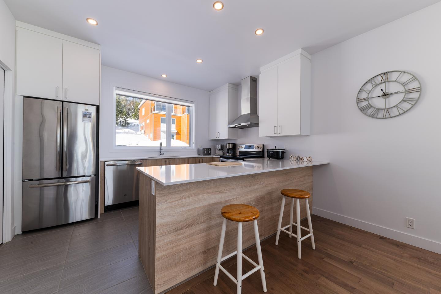 Cuisine moderne blanche avec un îlot en bois, tabourets et grande fenêtre.