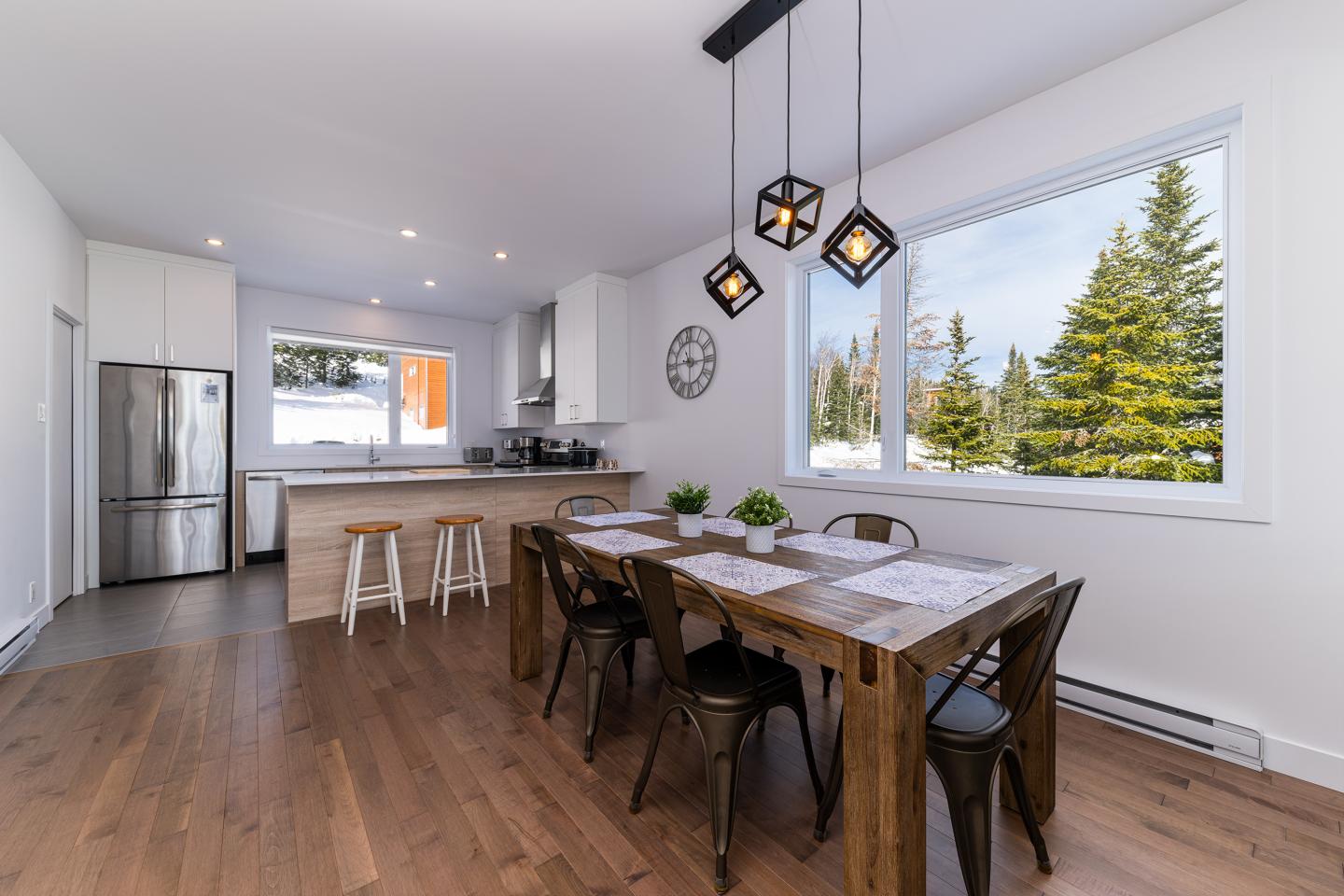 Cuisine moderne avec table en bois, fenêtres donnant sur des arbres.