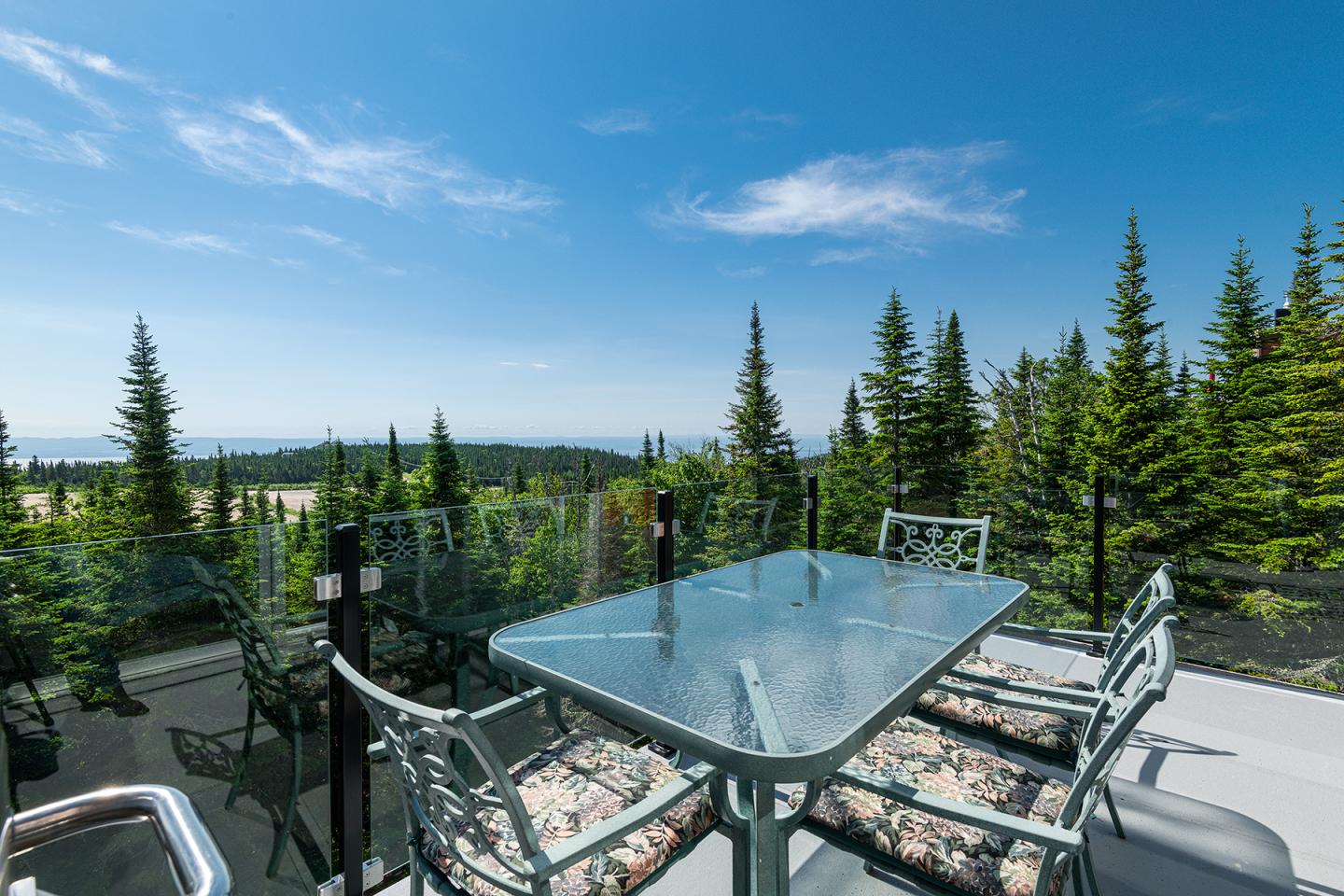 Table en verre sur une terrasse avec vue sur forêt et ciel bleu.