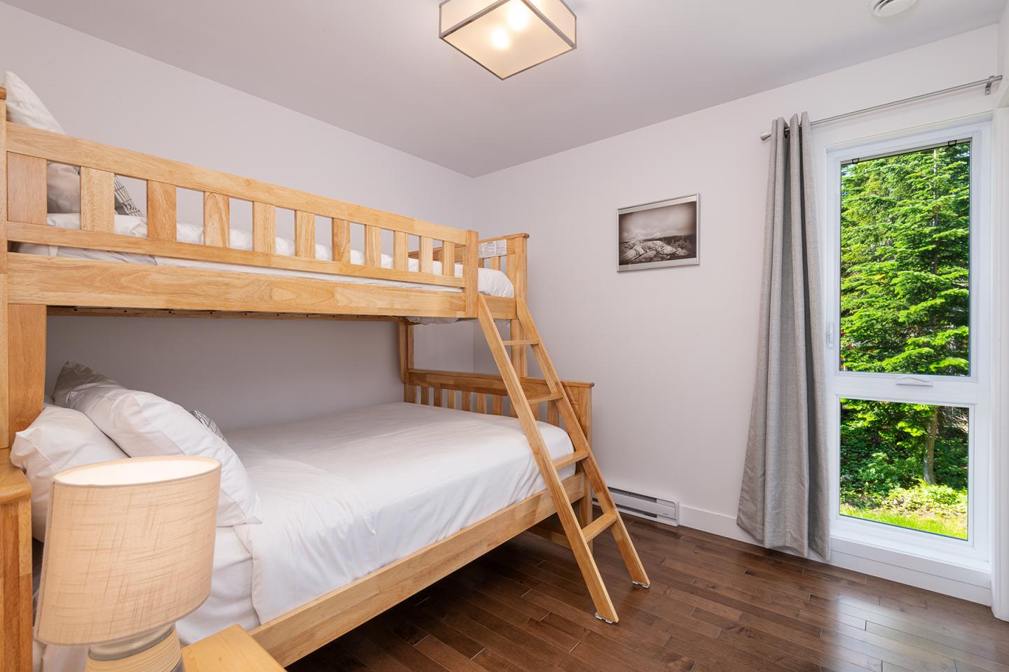 Chambre lumineuse avec lits superposés en bois, grande fenêtre, et parquet.