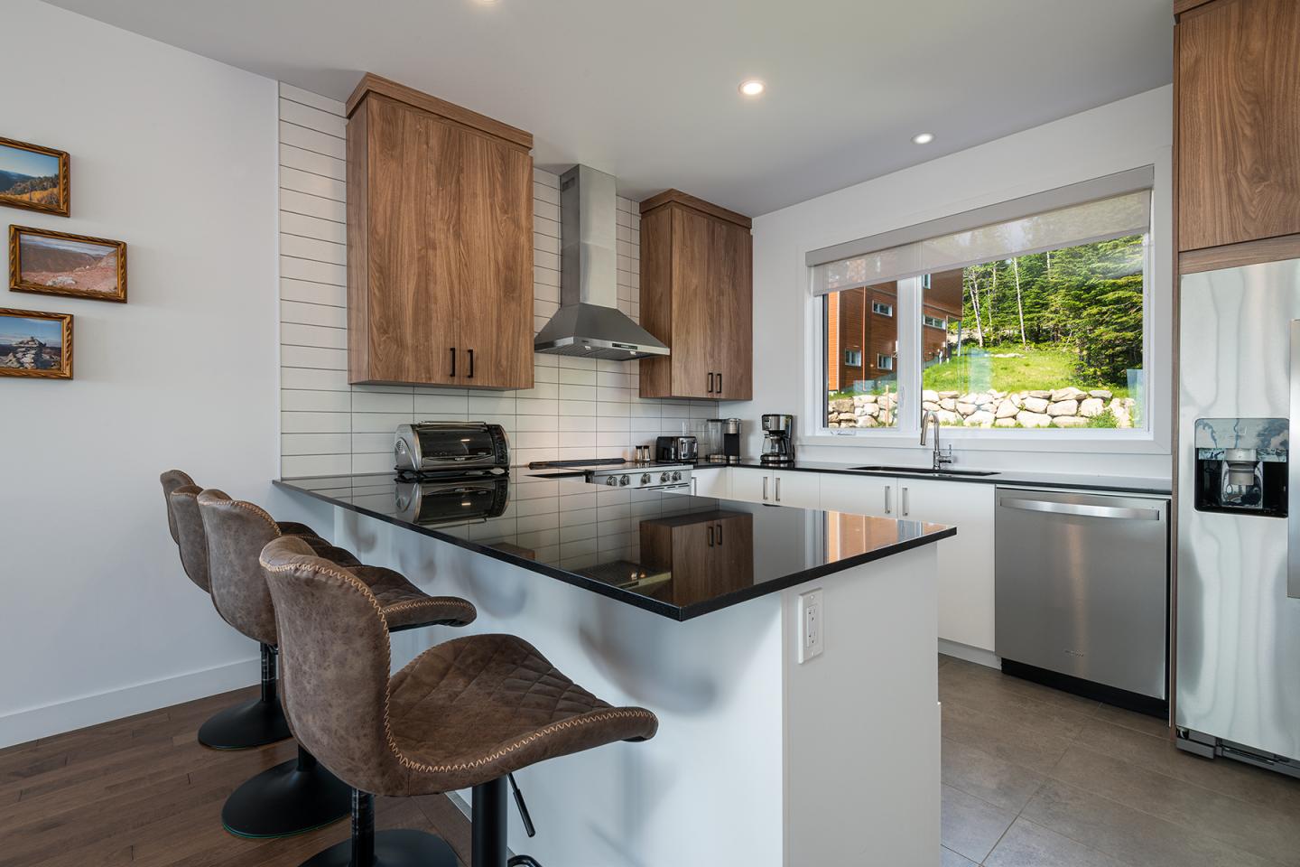 Cuisine moderne avec îlot central, tabourets marron, placards en bois et électroménager inox.