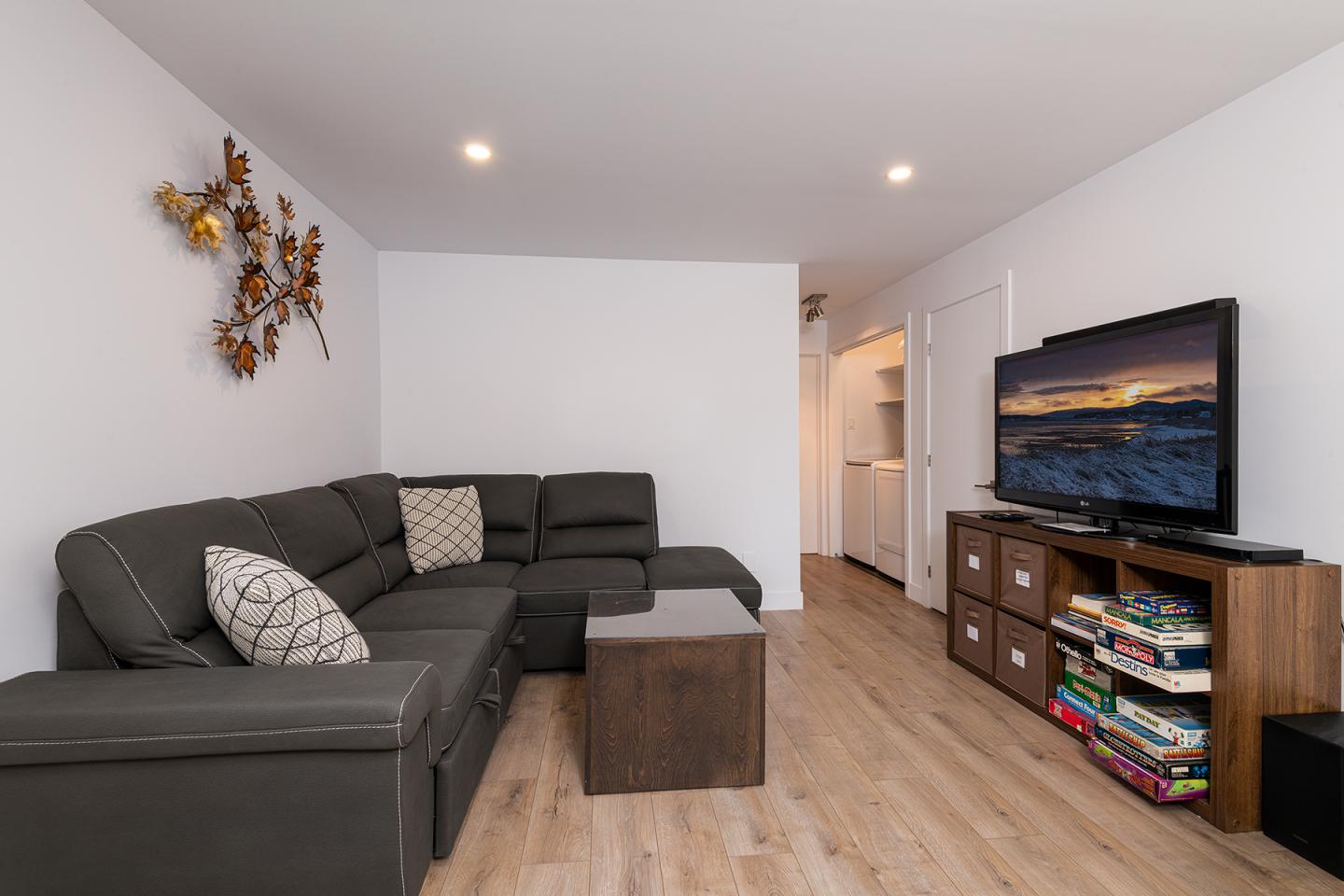 Salon moderne avec canapé gris, télévision, et sol en bois clair.