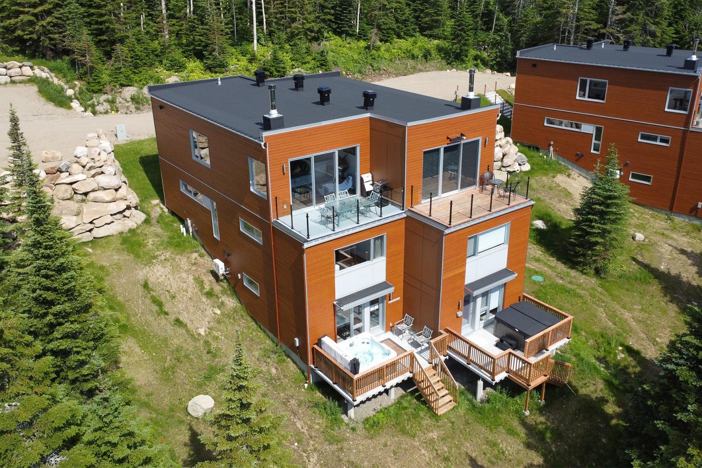 Maison moderne en bois avec terrasses, entourée d'arbres et de pelouses vertes.