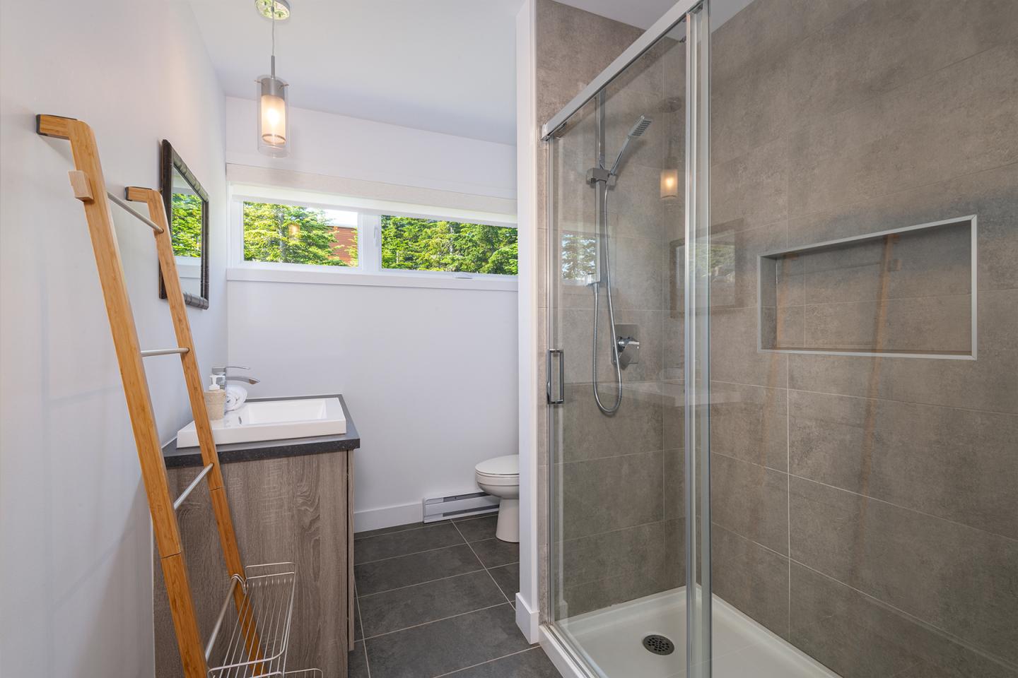 Salle de bain moderne avec douche en verre et mur gris, lavabo à gauche.