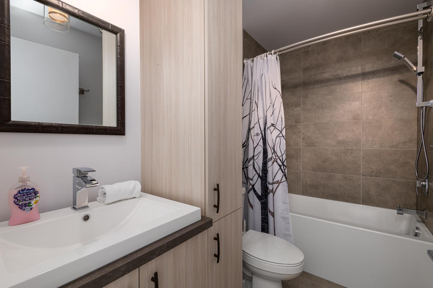Salle de bain moderne avec lavabo, miroir, douche et rideau imprimé d'arbres.