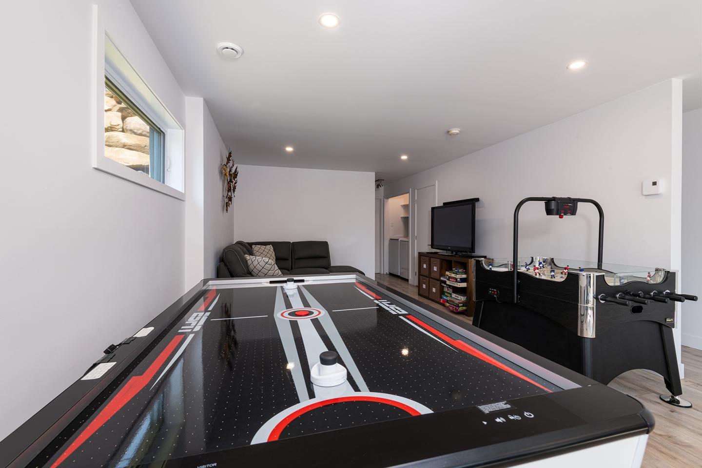 Salle de jeux avec air hockey, canapé gris et télé.