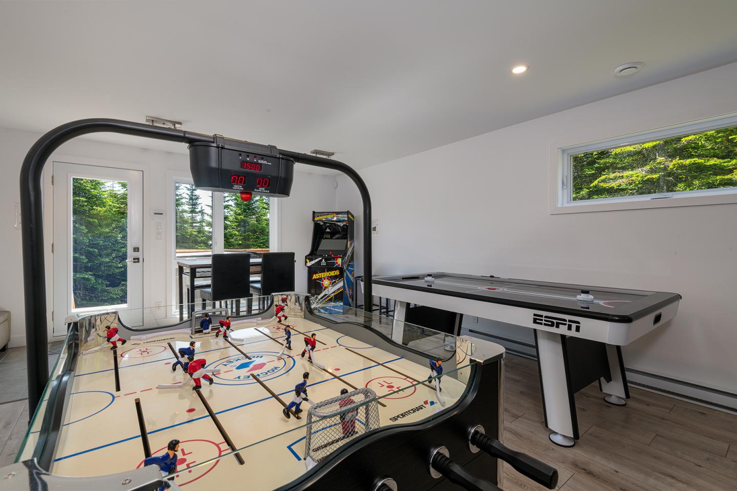 Salle de jeux avec tables de hockey et de air hockey, fenêtre et porte vitrée.