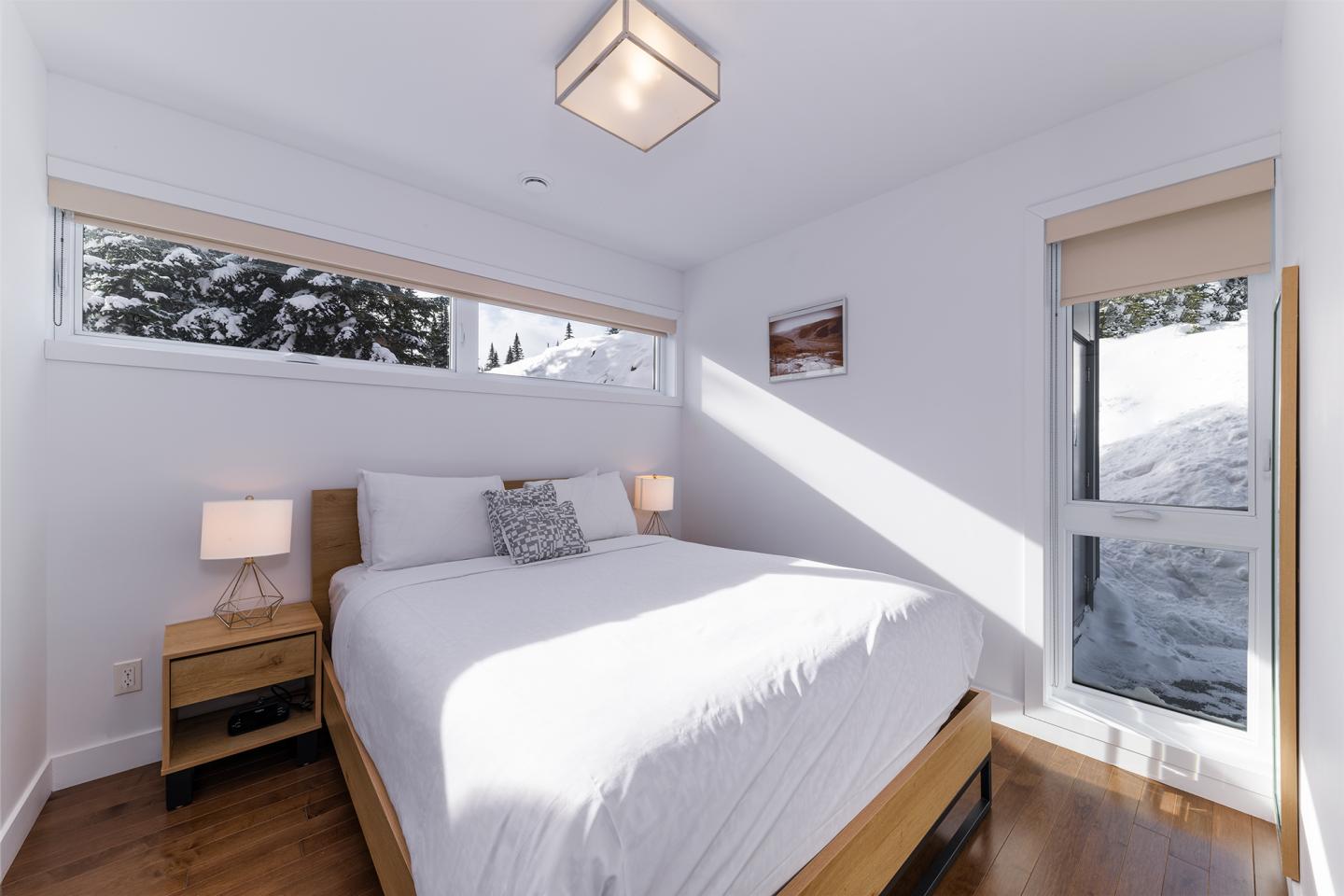 Chambre lumineuse avec un lit double, deux lampes et vue sur la neige par la fenêtre.