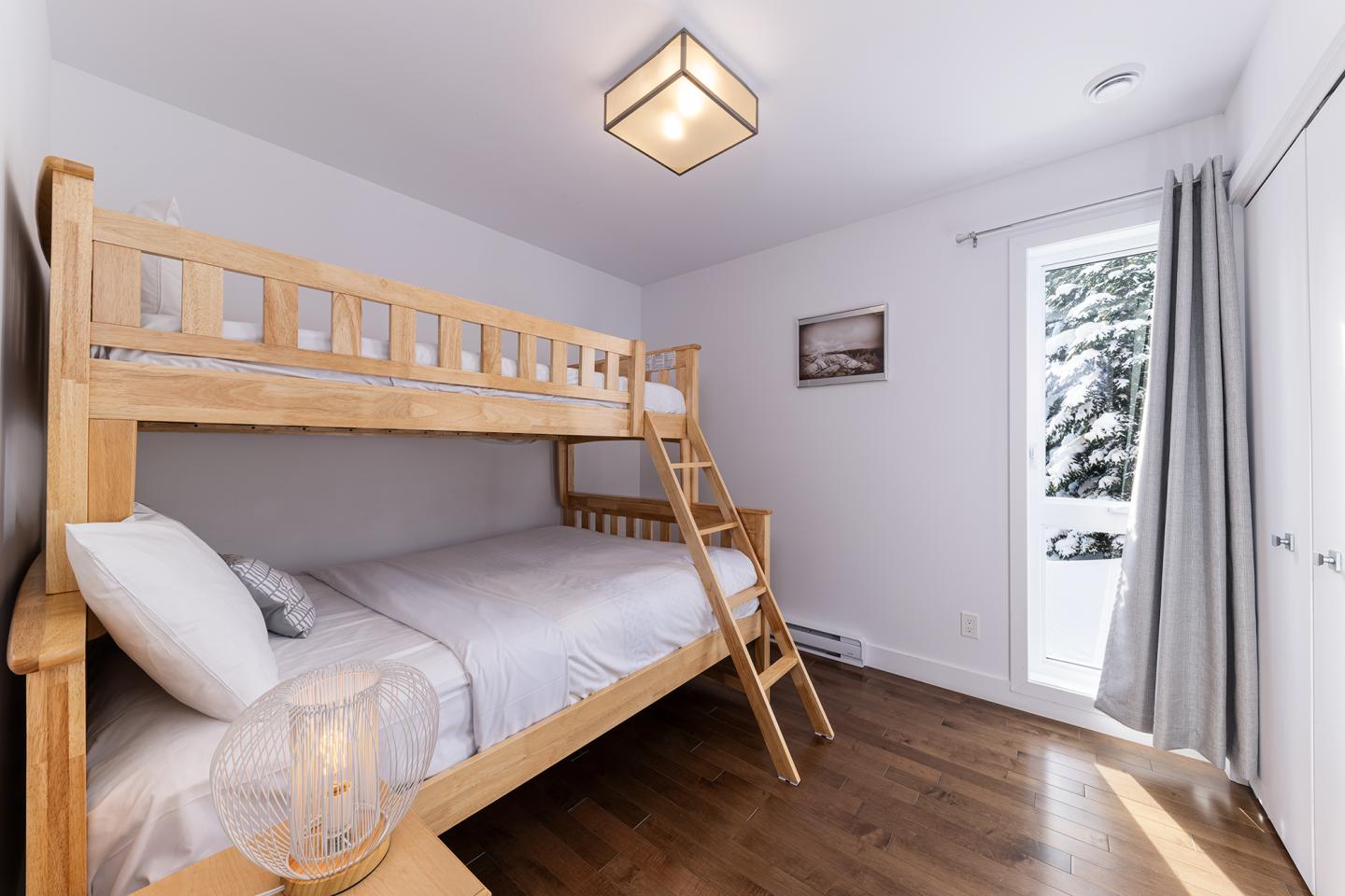 Chambre lumineuse avec lits superposés en bois, rideaux blancs et vue sur la neige.
