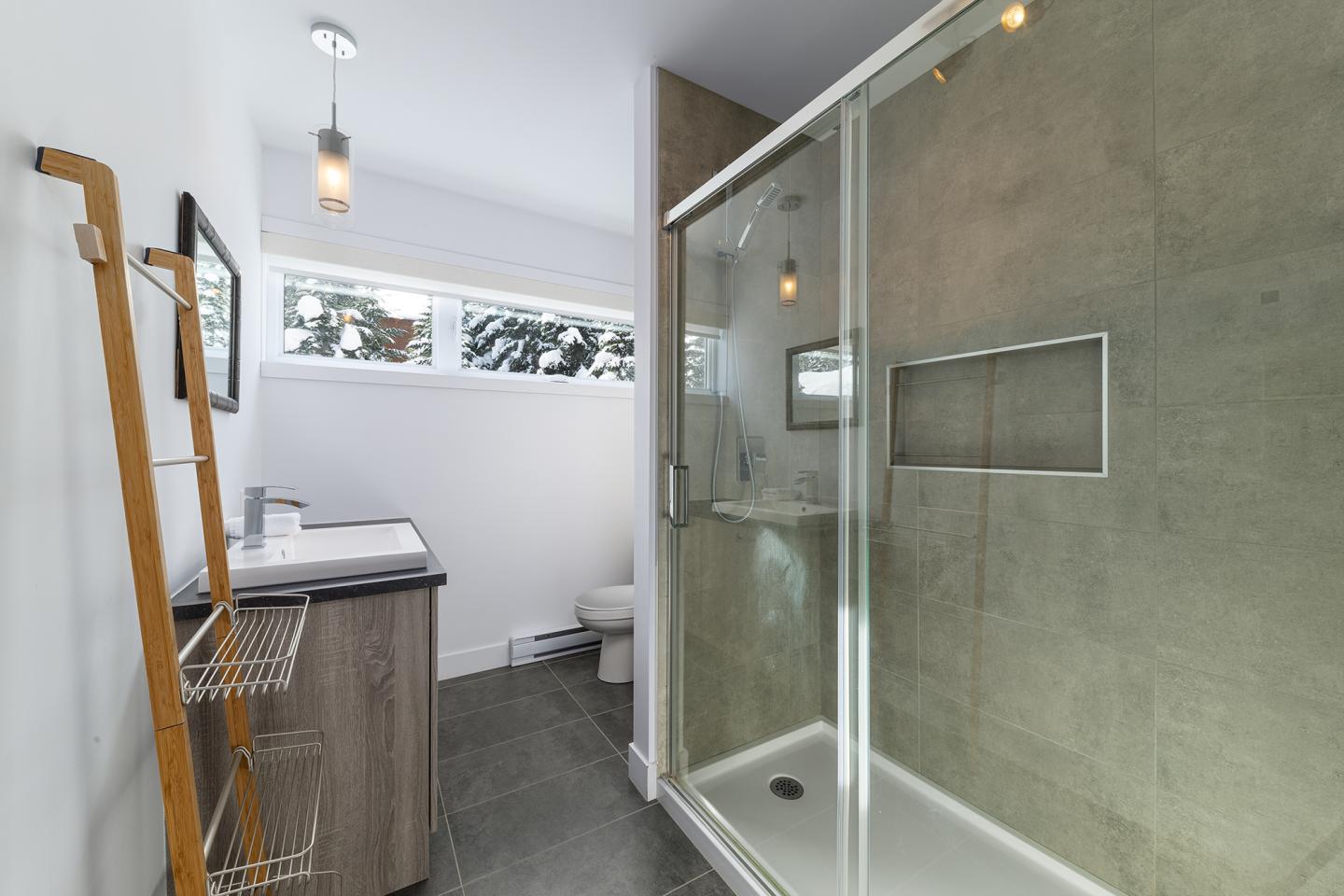 Salle de bain moderne avec douche vitrée et lavabo, éclairage suspendu.