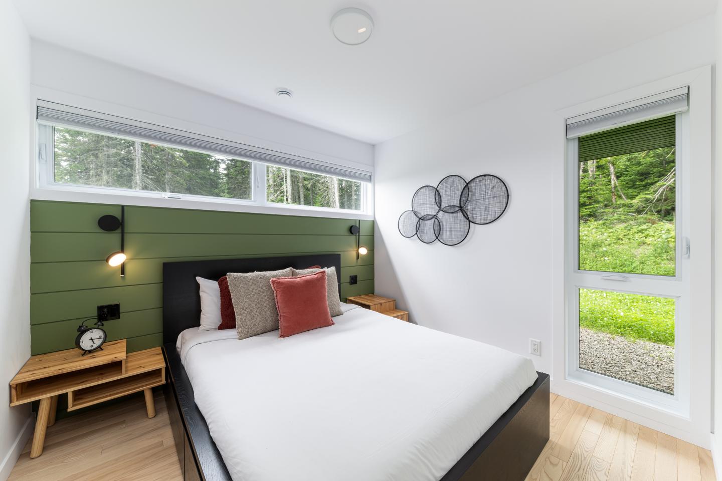 Chambre moderne avec lit double, oreillers rouges, fenêtres et vue sur le jardin.