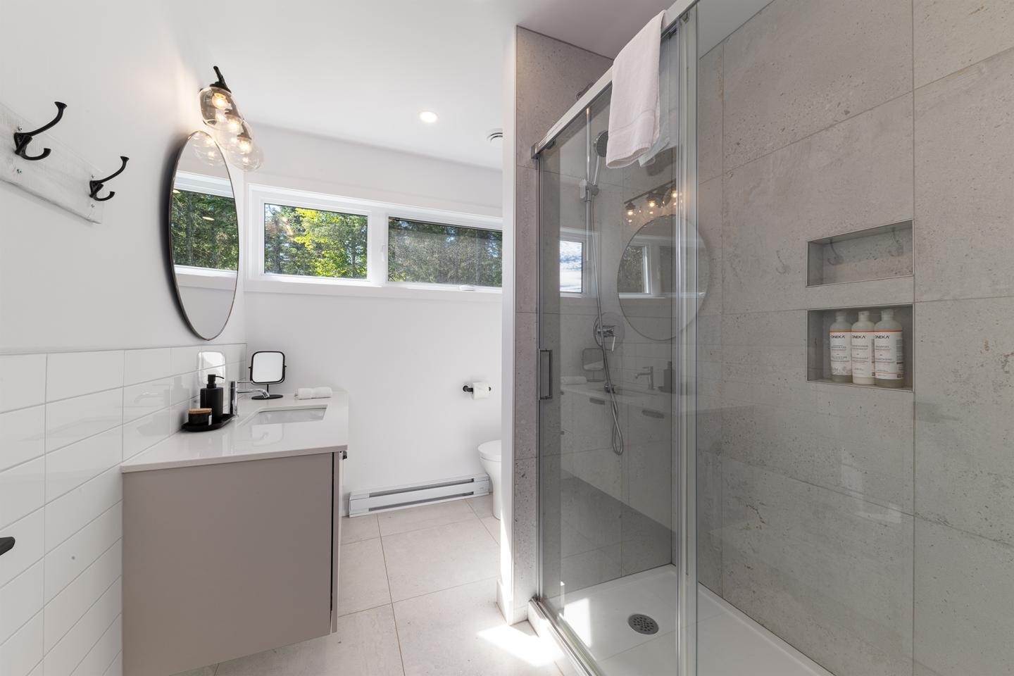 Salle de bain moderne, douche vitrée et lavabo avec miroir rond.