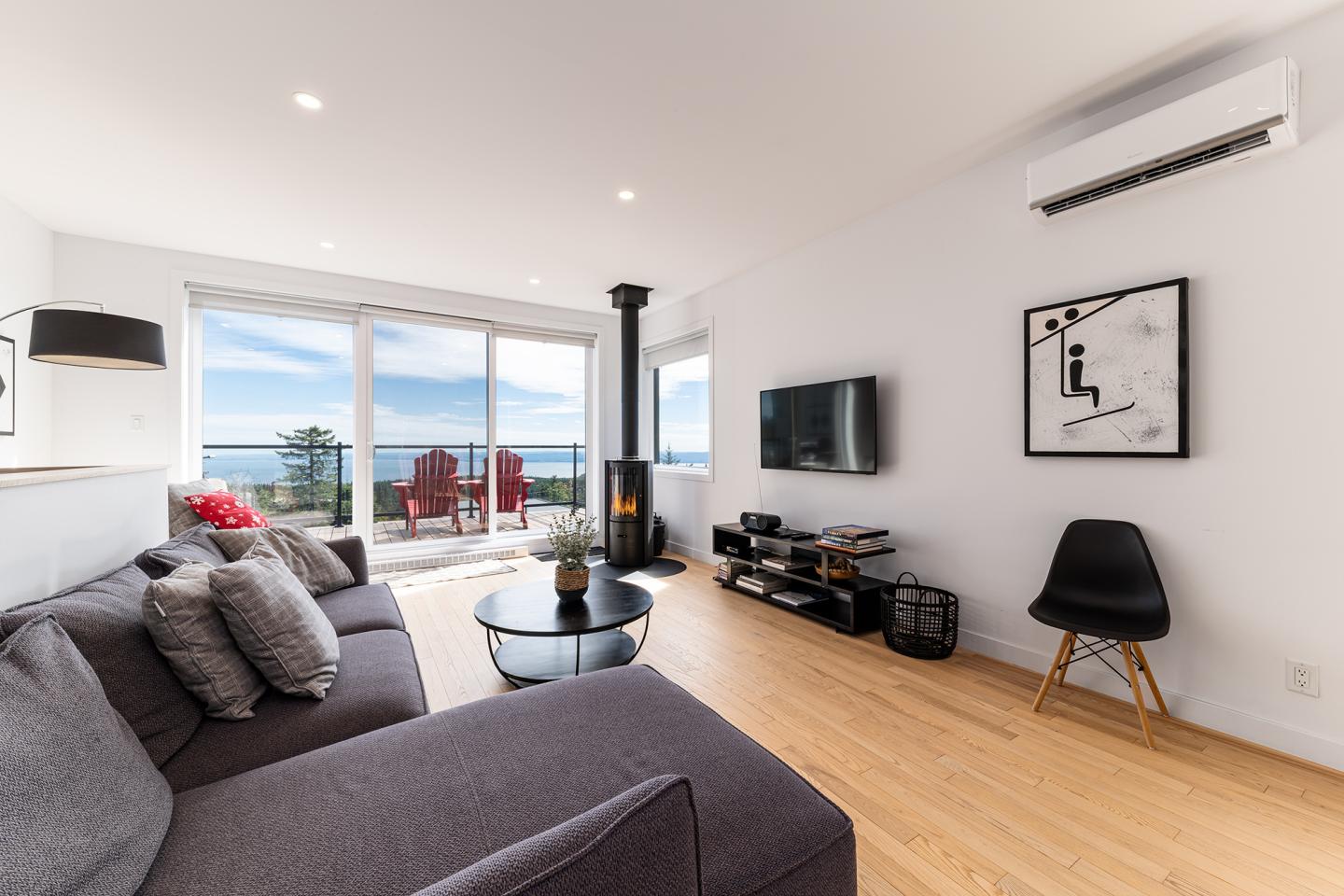 Salon moderne avec vue océan, canapé gris, table basse et décoration minimaliste.
