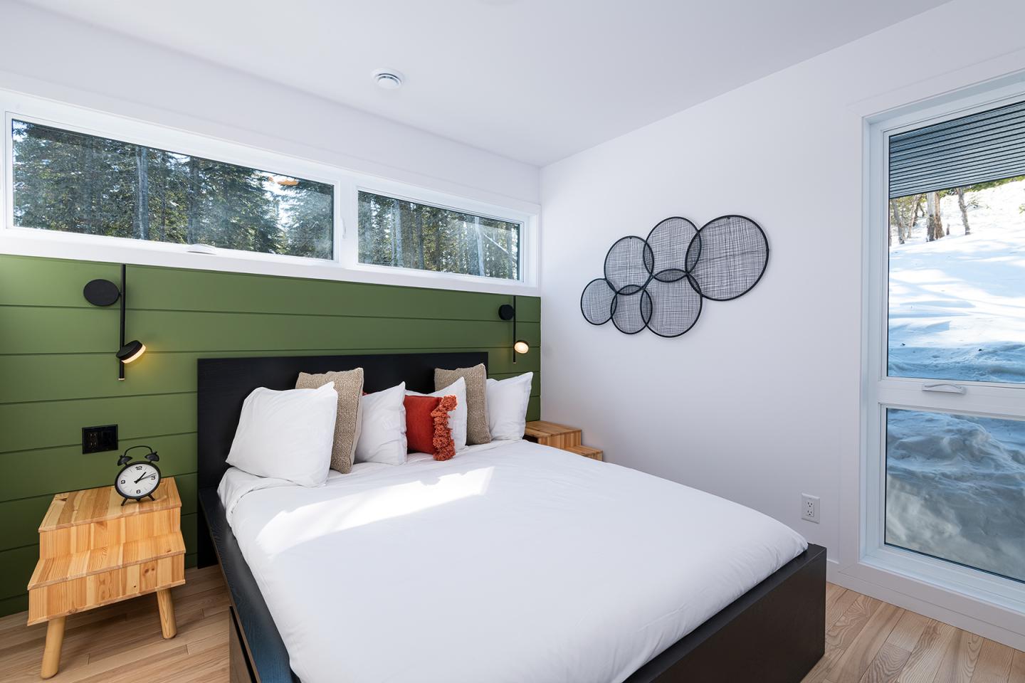 Chambre moderne avec lit blanc, mur vert et grande fenêtre enneigée.