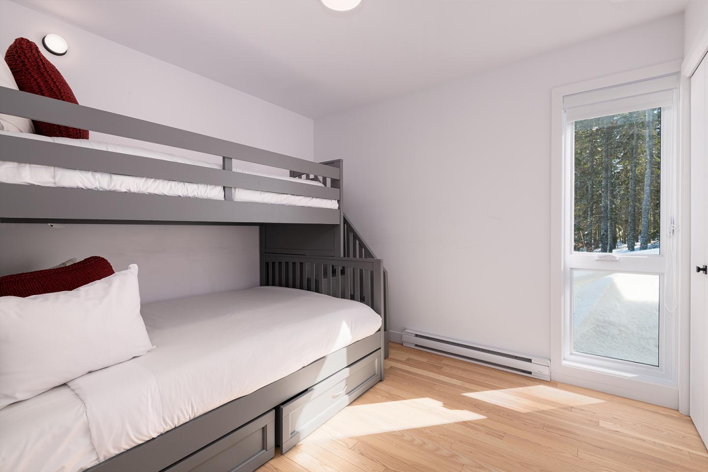 Chambre lumineuse avec lits superposés gris et coussins rouges, parquet clair.