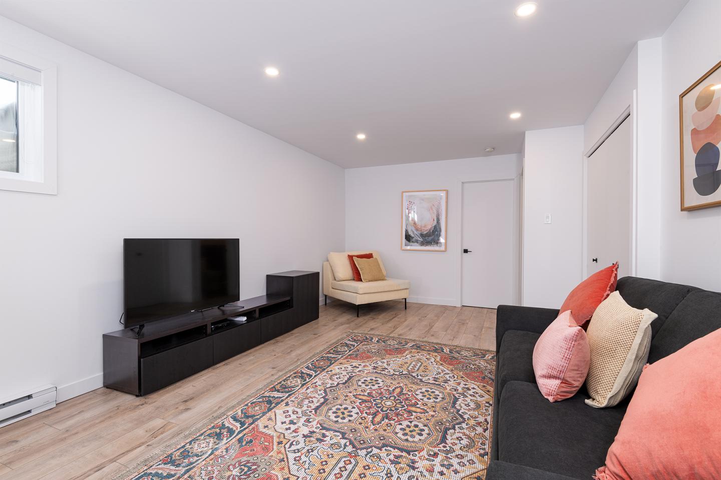 Salon moderne avec canapé gris, coussins colorés, télé et tapis oriental.