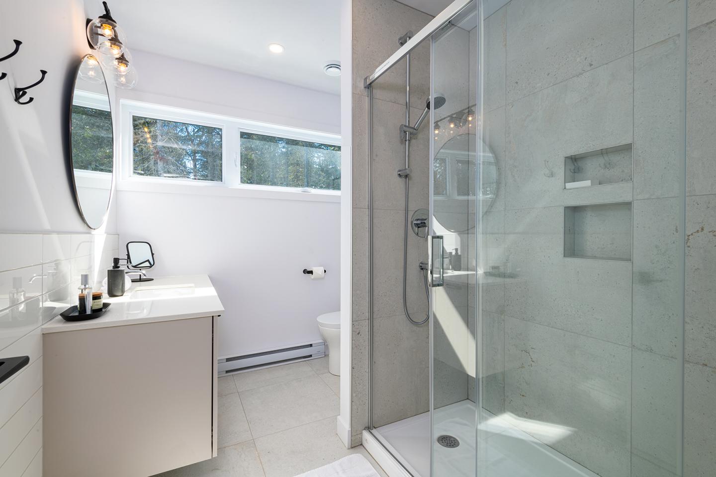 Salle de bain moderne avec douche vitrée et lavabo. Lumineux avec mur blanc et fenêtre.