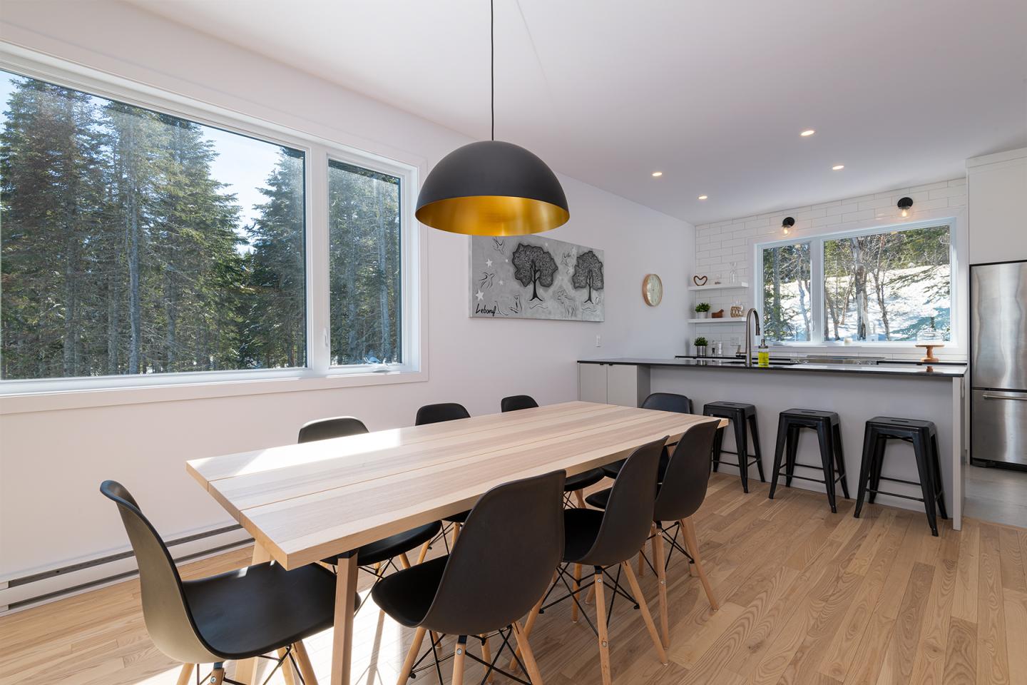 Salle à manger moderne avec table en bois, chaises noires, et vue sur la forêt.