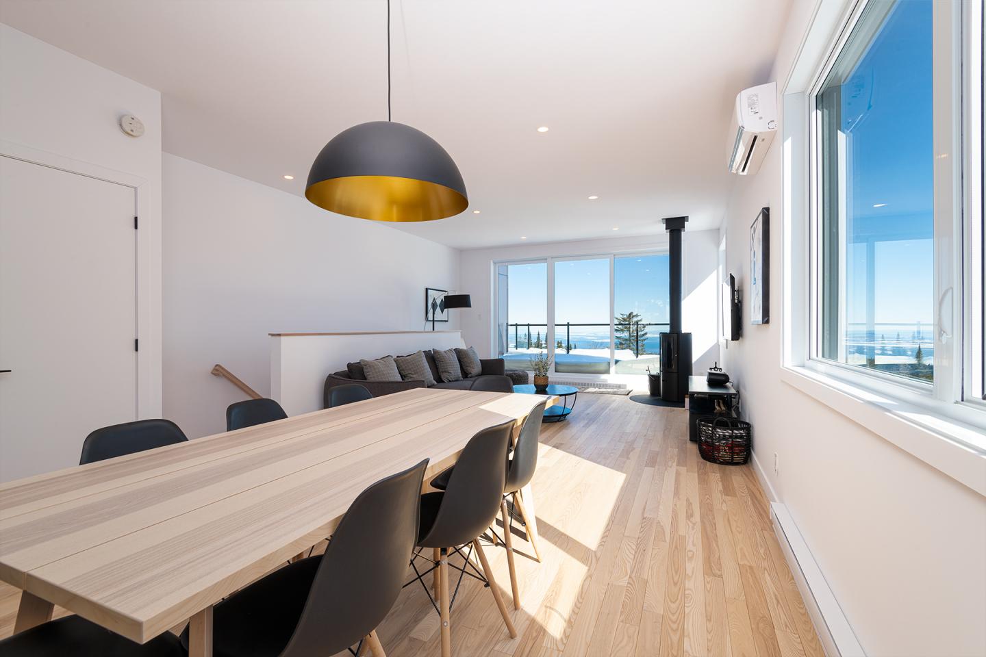 Salle à manger moderne, table en bois, grande fenêtre vue mer.