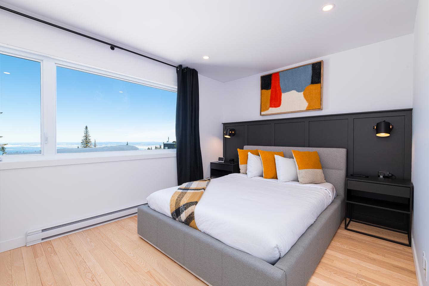 Chambre moderne avec lit, grande fenêtre et tableau coloré au mur.