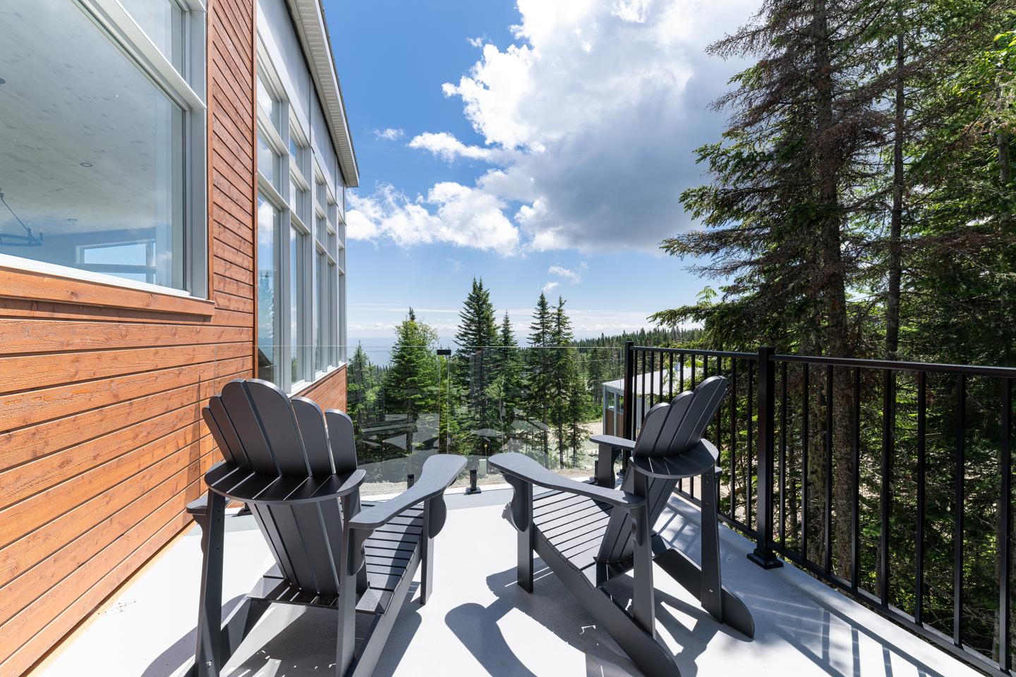 Terrasse ensoleillée avec chaises Adirondack, vue sur forêt, ciel bleu.