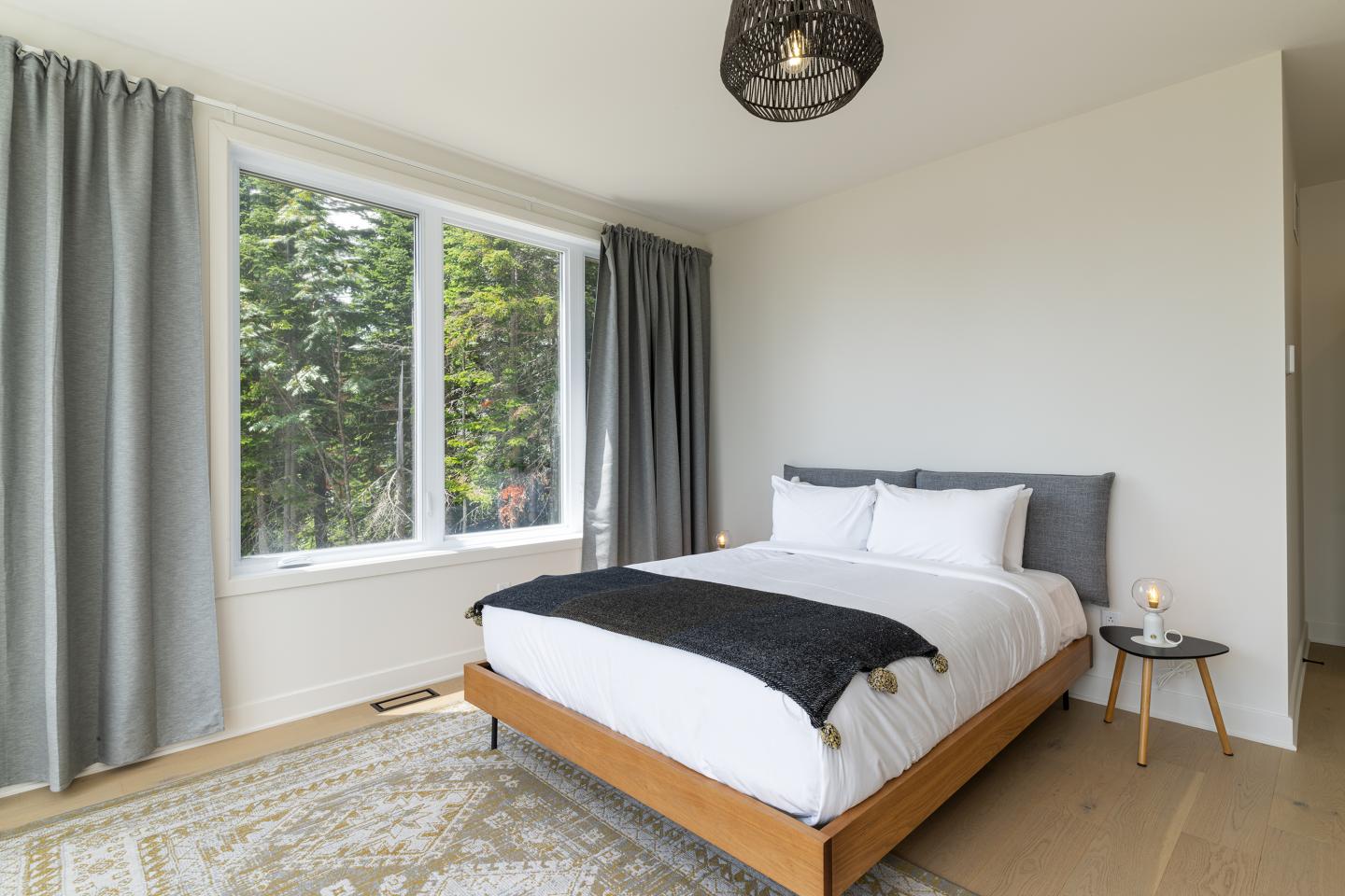 Chambre lumineuse avec lit double, grandes fenêtres et rideaux gris.