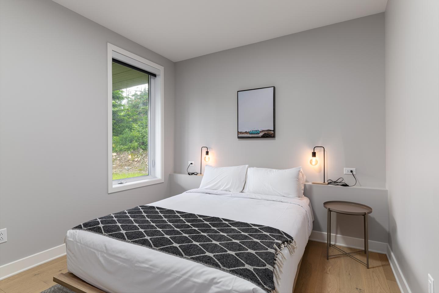 Chambre minimaliste avec lit double, lampe murale et cadre.