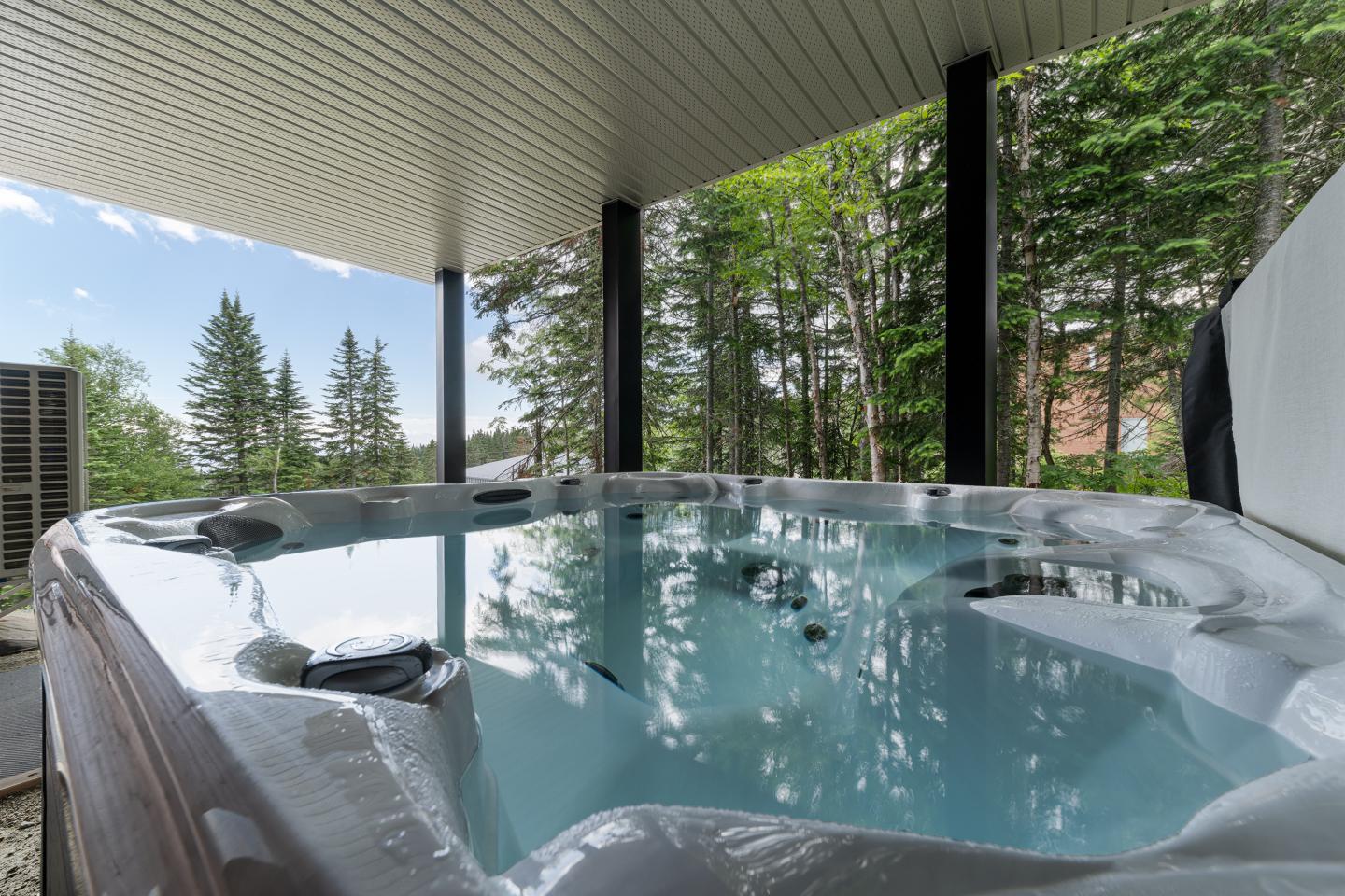 Jacuzzi sous un auvent, entouré de forêt verdoyante.