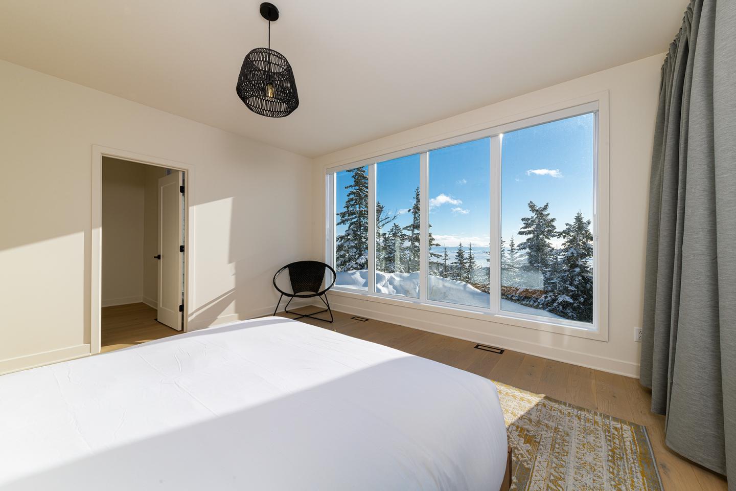 Chambre lumineuse avec grande fenêtre, vue sur la neige et les arbres.